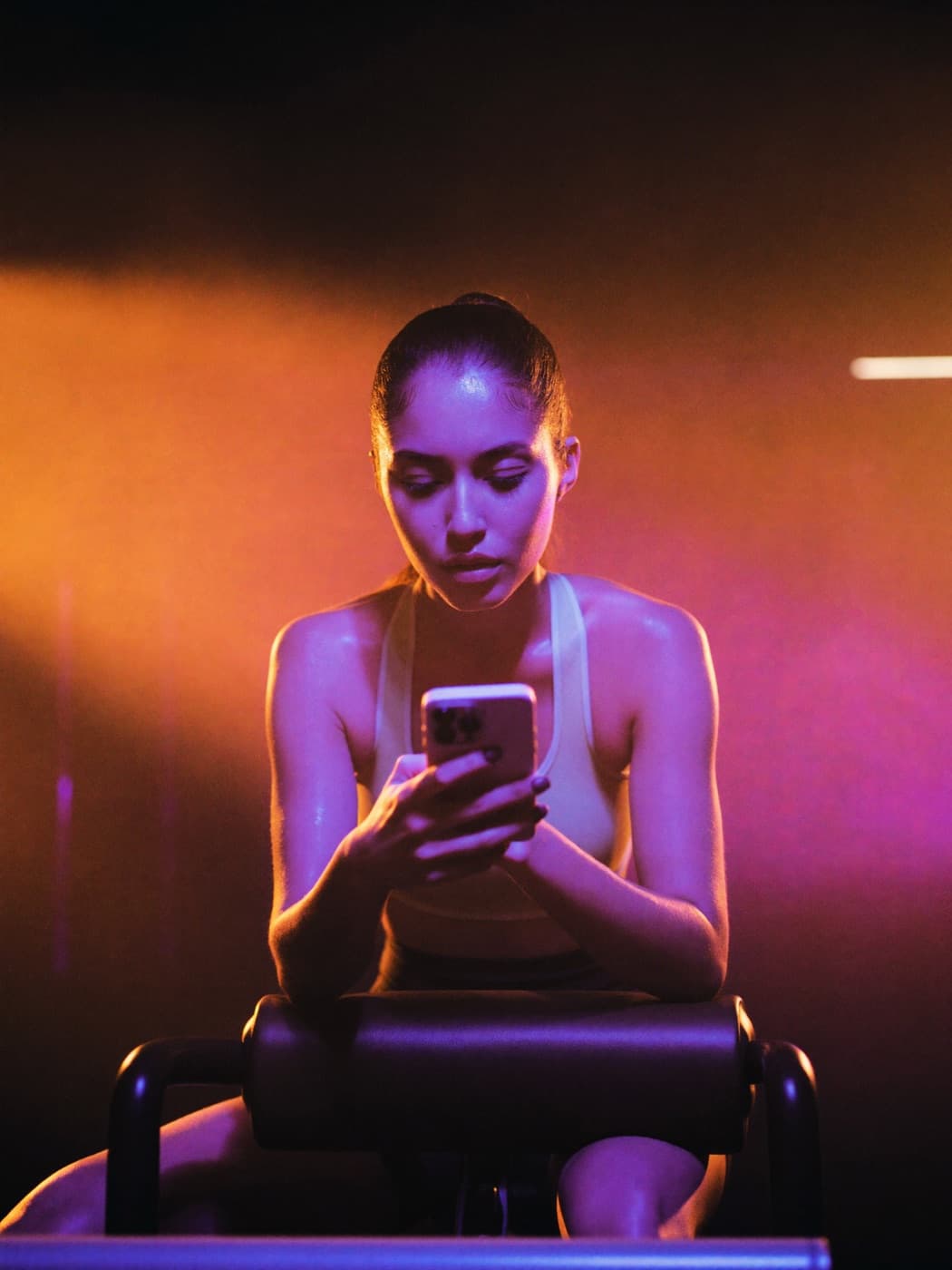 Athlete checking her workout on a phone mid-session in a moody gym